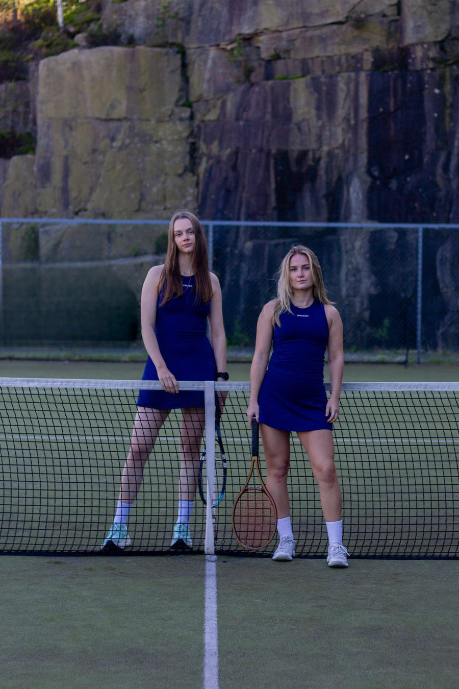 Two women in navy Dessard Maya dresses on a tennis court